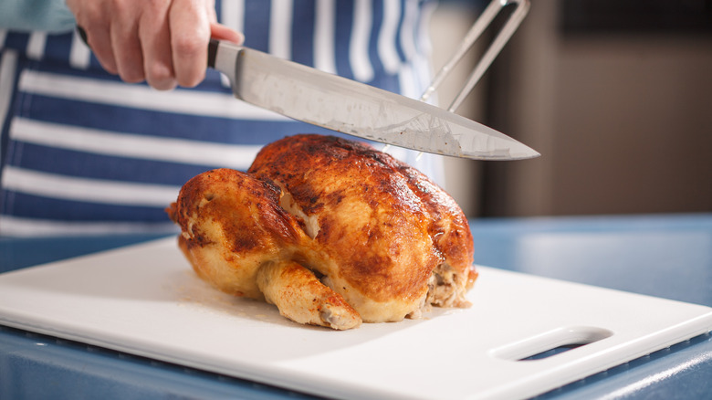 Hands slicing rotisserie chicken on cutting board
