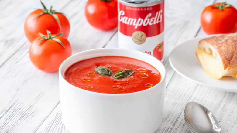 Bowl of tomato soup with basil and bread, and Campbell's soup can in background