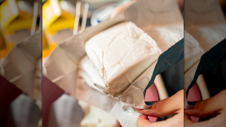 Hands unwrapping a block of cream cheese