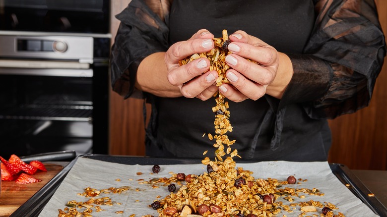 Hands mixing homemade granola on baking sheet