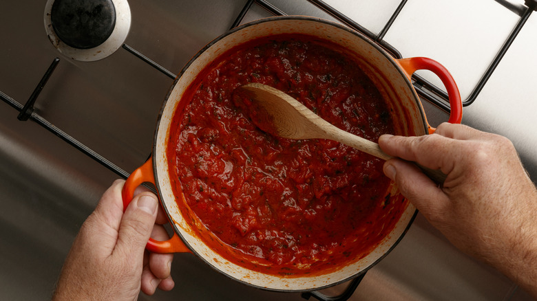 Hands stirring pot of tomato sauce