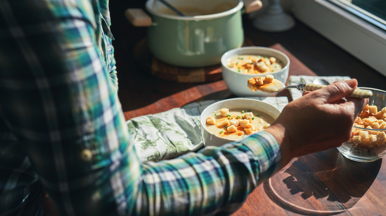 Person eating bowl of soup with soup pot in background