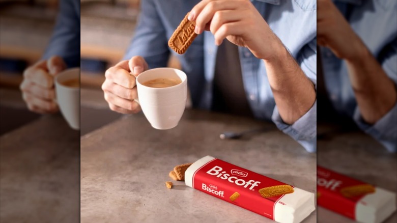 Hands holding a Lotus Biscoff cookie over a cup of coffee near a whole pack of cookies