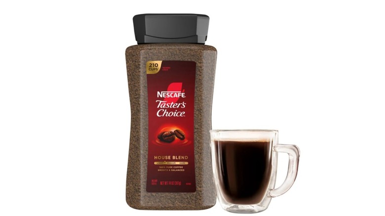 Container of Nescafe instant coffee and a clear mug of coffee on white background