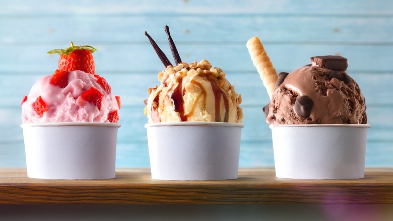strawberry ice cream, vanilla ice cream with caramel and nuts, and chocolate ice cream in paper cups on on a counter