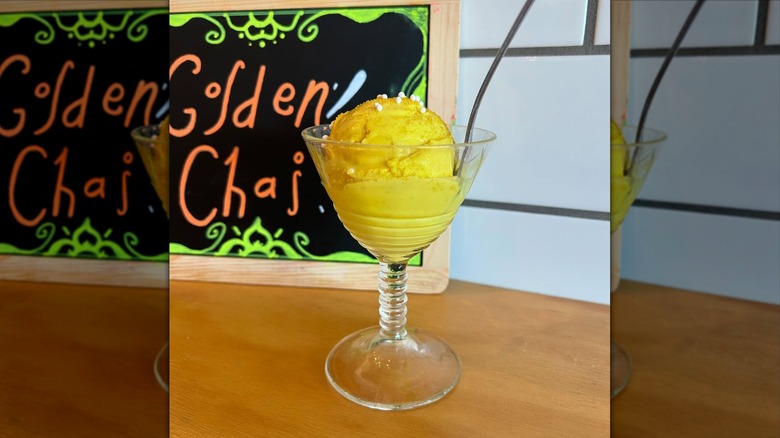 A glass dish of golden chai ice cream on counter in front of chalkboard sign at La Lecheria ice cream parlor