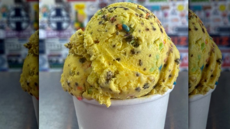 yellow ice cream with cookie pieces and rainbow candies in a white paper cup from Max and Mina's