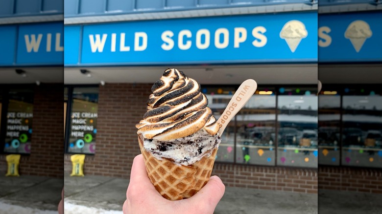 Cookies and cream ice cream topped with torched marshmallow fluff in waffle cone in front of Wild Scoops ice cream parlor