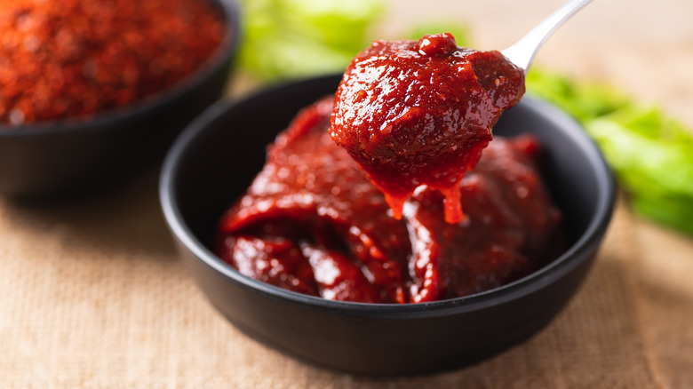 Spoon lifting gochujang from black dish