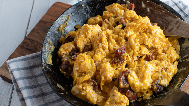 scrambled eggs with chorizo in a black frying pan on a blue and white checked napkin over a wooden board