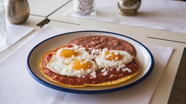 huevos rancheros on a white plate with a blue rim sitting on a kitchen counter