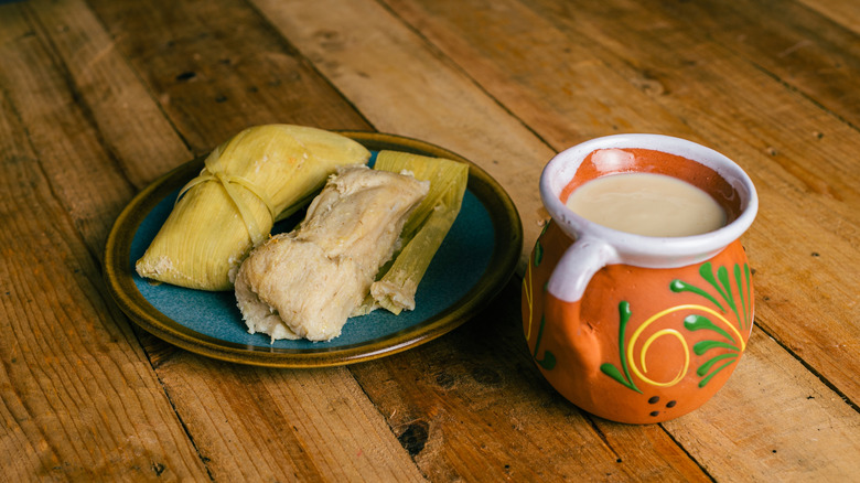 tamales on a blue plate with atole in an orange cup on a wooden table