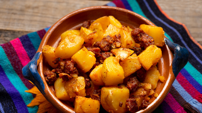 potatoes with chorizo in a brown bowl on a brightly colored striped napkin