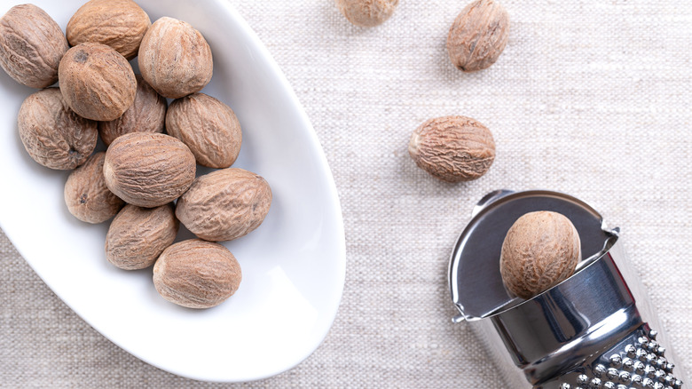 Whole nutmeg in a dish next to a grater
