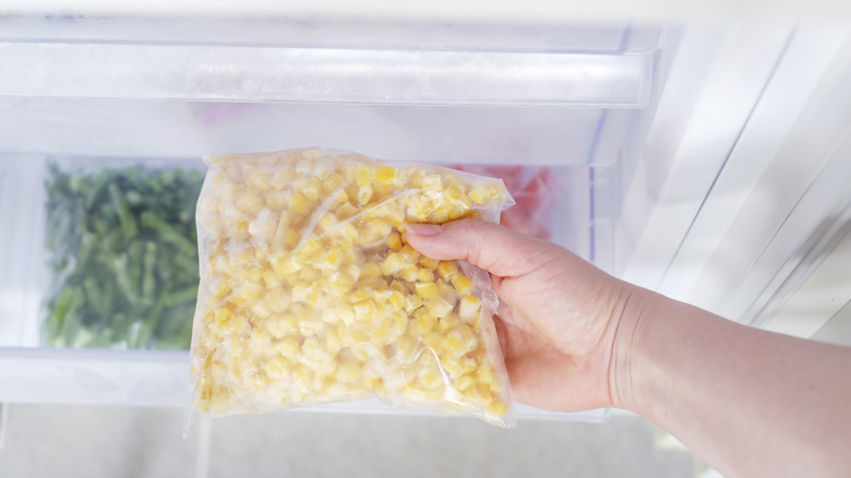 Hand pulling frozen corn out of fridge
