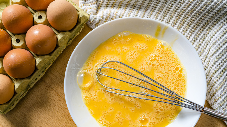 Bowl of raw eggs with whisk