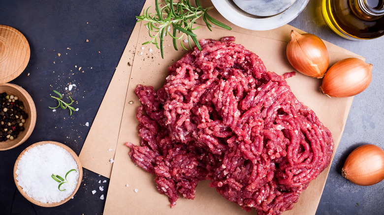 Lean ground beef on parchment paper with ingredients surrounding it