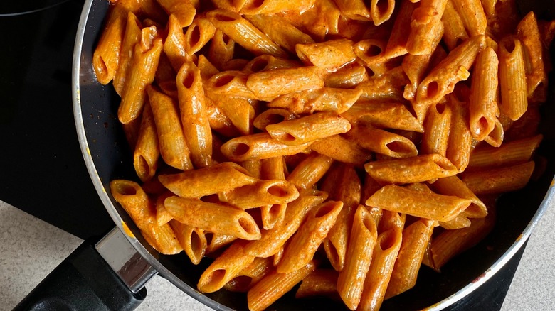 Penne alla vodka in a creamy sauce cooking in a black pan