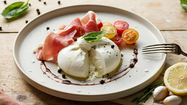 Burrata with cheese, tomatoes, and ham on a white plate