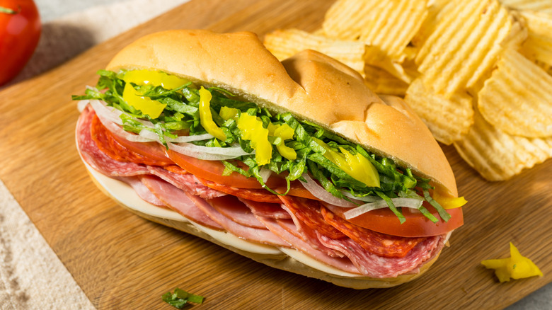 Italian sub with meats, veggies, and cheese sits on a cutting board