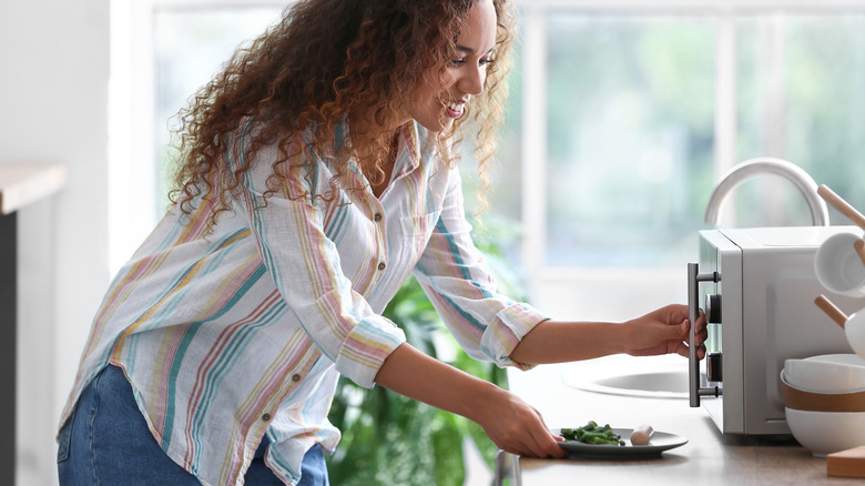 Person putting vegetables into microwave