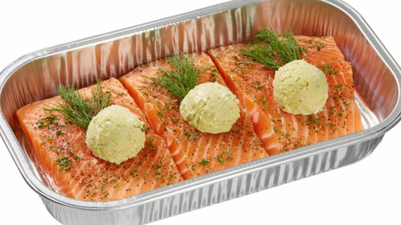 An aluminum pan filled with three Kirkland Signature salmon Milano with pesto butter and herbs on top.
