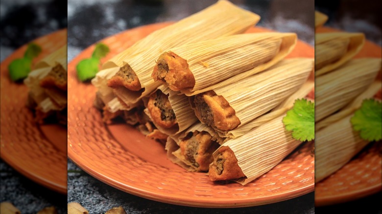 A pile of Texas tamales on an orange plate with cilantro garnish.