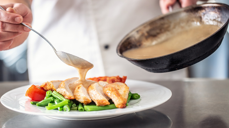 Chef spooning a sauce over chicken and vegetables