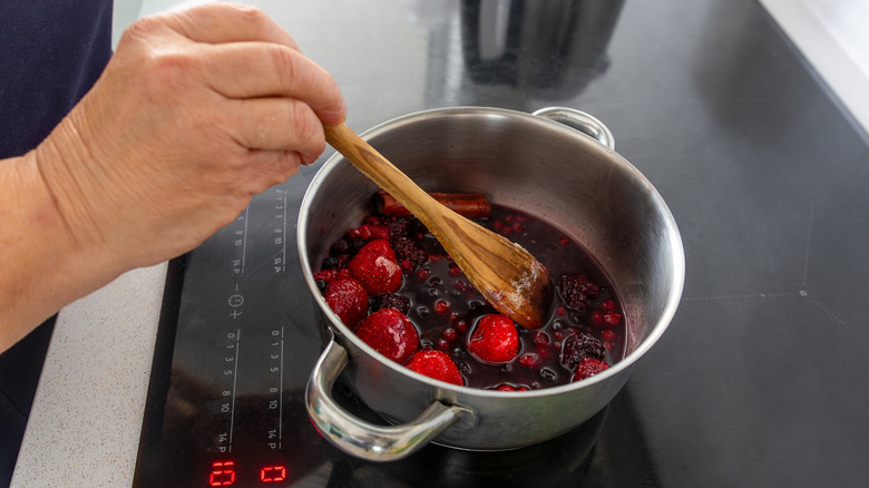 Hand stirring fruit in pot on stove with wooden spoon