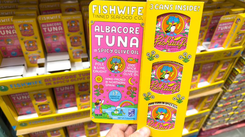 Hand holding cans of tuna in olive oil at store