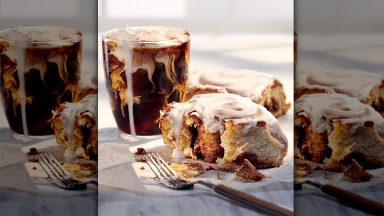 cinnamon rolls next to a glass cup of coffee with milk