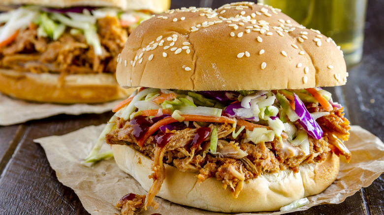 A close-up of a barbecue chicken sandwich with slaw on it with a beer and a second sandwich in the background