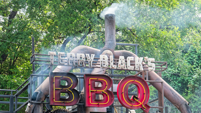 A Terry Black's BBQ sign attached to a meat smoker with smoke billowing out the top