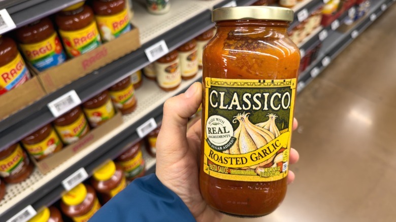 A hand holding a jar of Classico Roasted Garlic sauce.