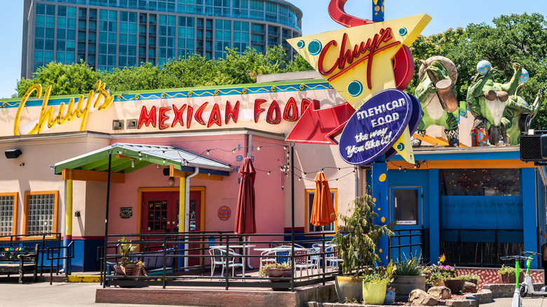 A colorful Chuy's with funky statues on the roof in a city location.