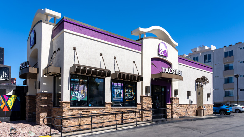 A Taco Bell in a standalone concrete building with a purple trim and clear blue skies behind it.