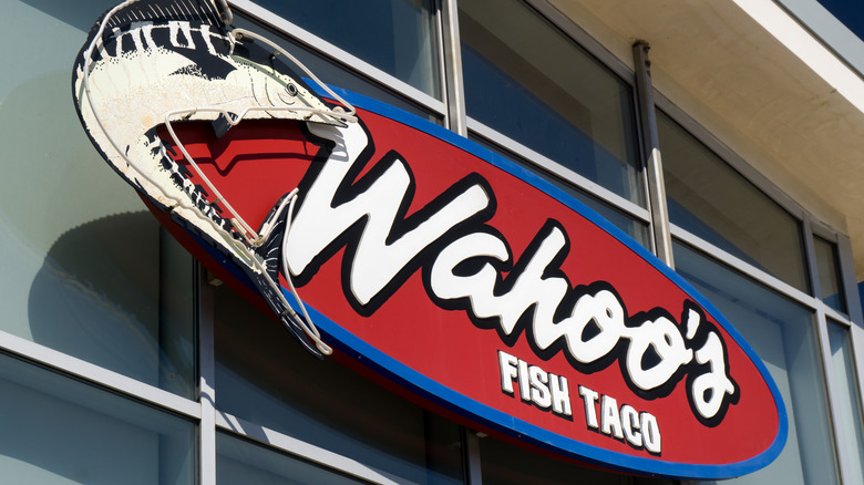 A red, surfboard shaped sign with Wahoo's written in large white cursive letters with a black outline.