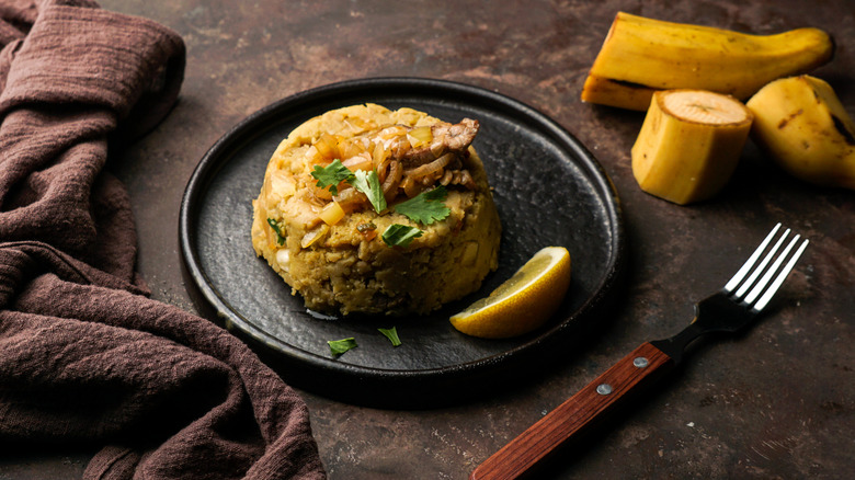 Mofongo, mashed boiled plantains with pork meat and onion, on plate with slice of lemon