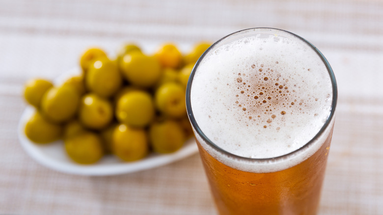 Glass of frothy beer with plate of olives