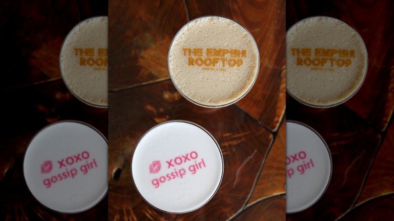 Two drinks with foam with Gossip Girl and The Empire Rooftop latte art spelled out