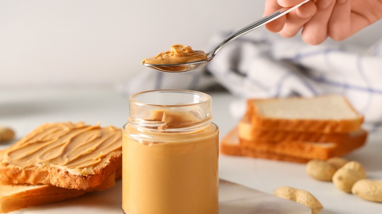 Hand taking a spoonful out of a  jar of peanut butter
