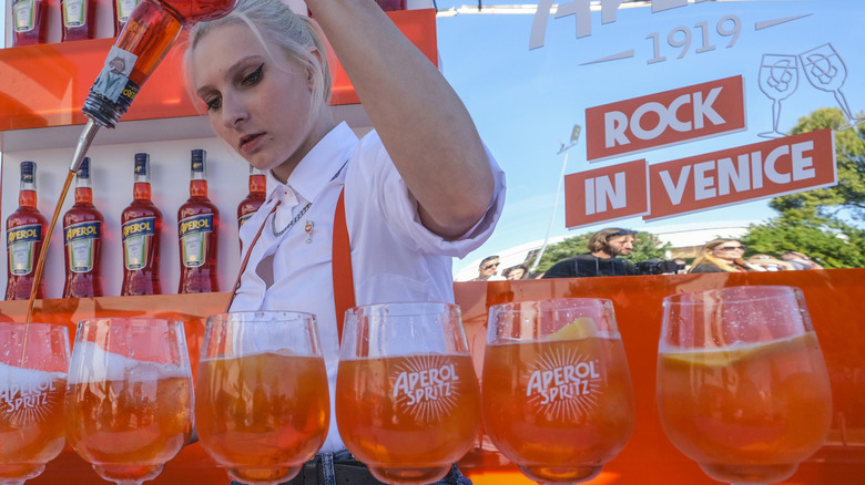 A bartender mixes a line of six Aperol spritz cocktails.