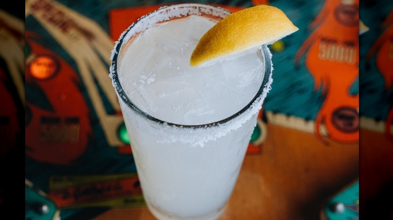 A clear liquid in highball glass with a salted rim and lemon wedge.