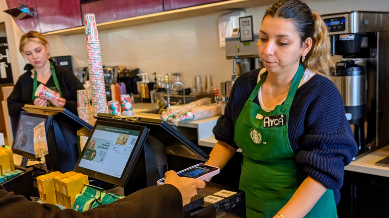 Starbucks worker taking payment from a customer while another prepares a drink order