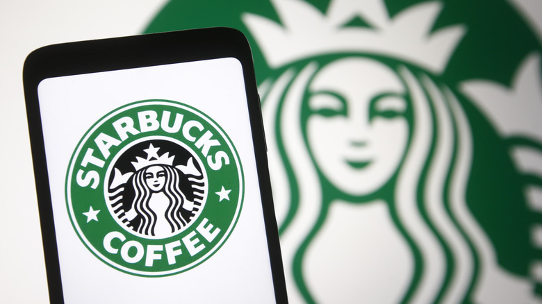 Starbucks logo on a phone screen in front of a bigger logo