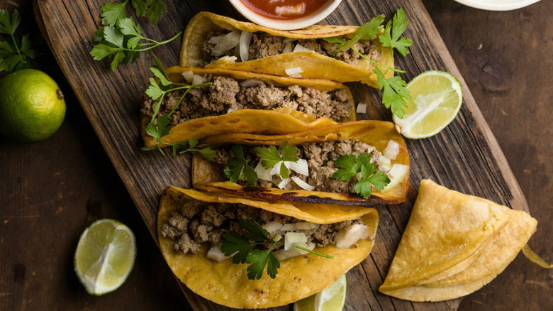 Birria tacos on wooden slab, served with lime and cilantro
