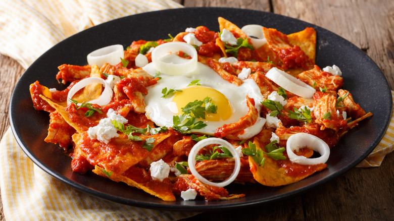 Black serving plate of chilaqiles topped with fried egg