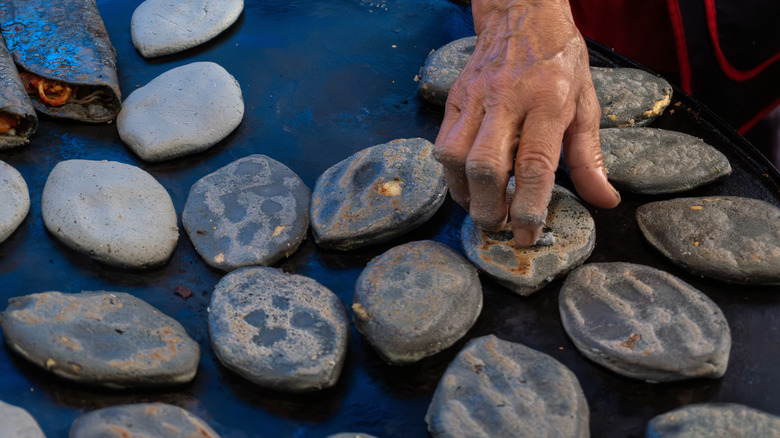 Blue corn tlacoyos on comal grill, hand turning them