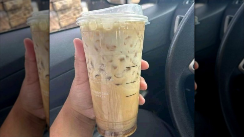 Hand holding Starbucks sweet cream based iced coffee drink in to go cup