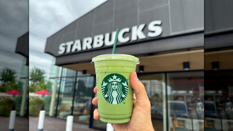 Hand holding a Starbucks iced matcha latte with storefront in the background